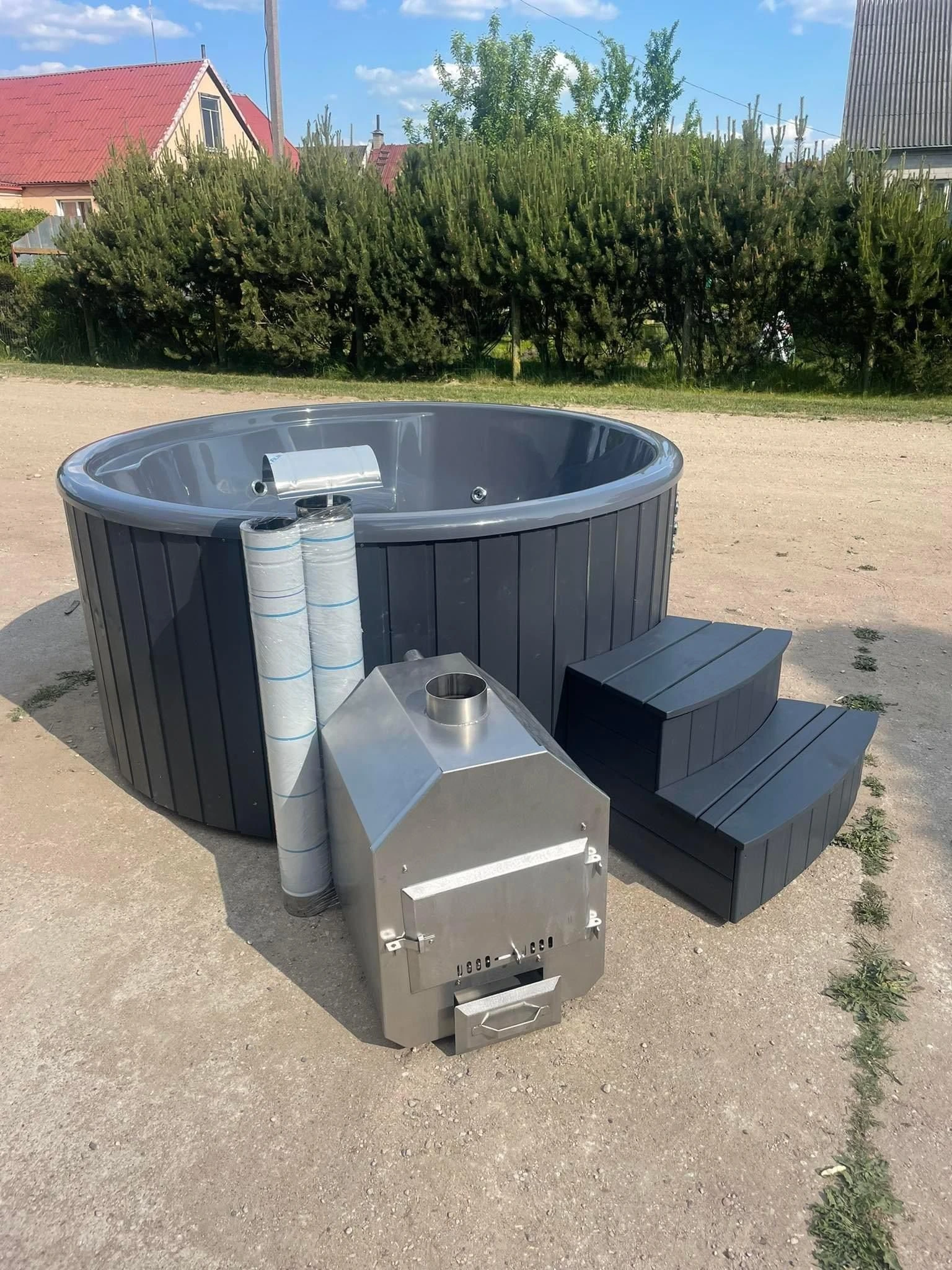 Mørk badestamp med grått kar, utvendig vedovn i rustfritt stål og trapp