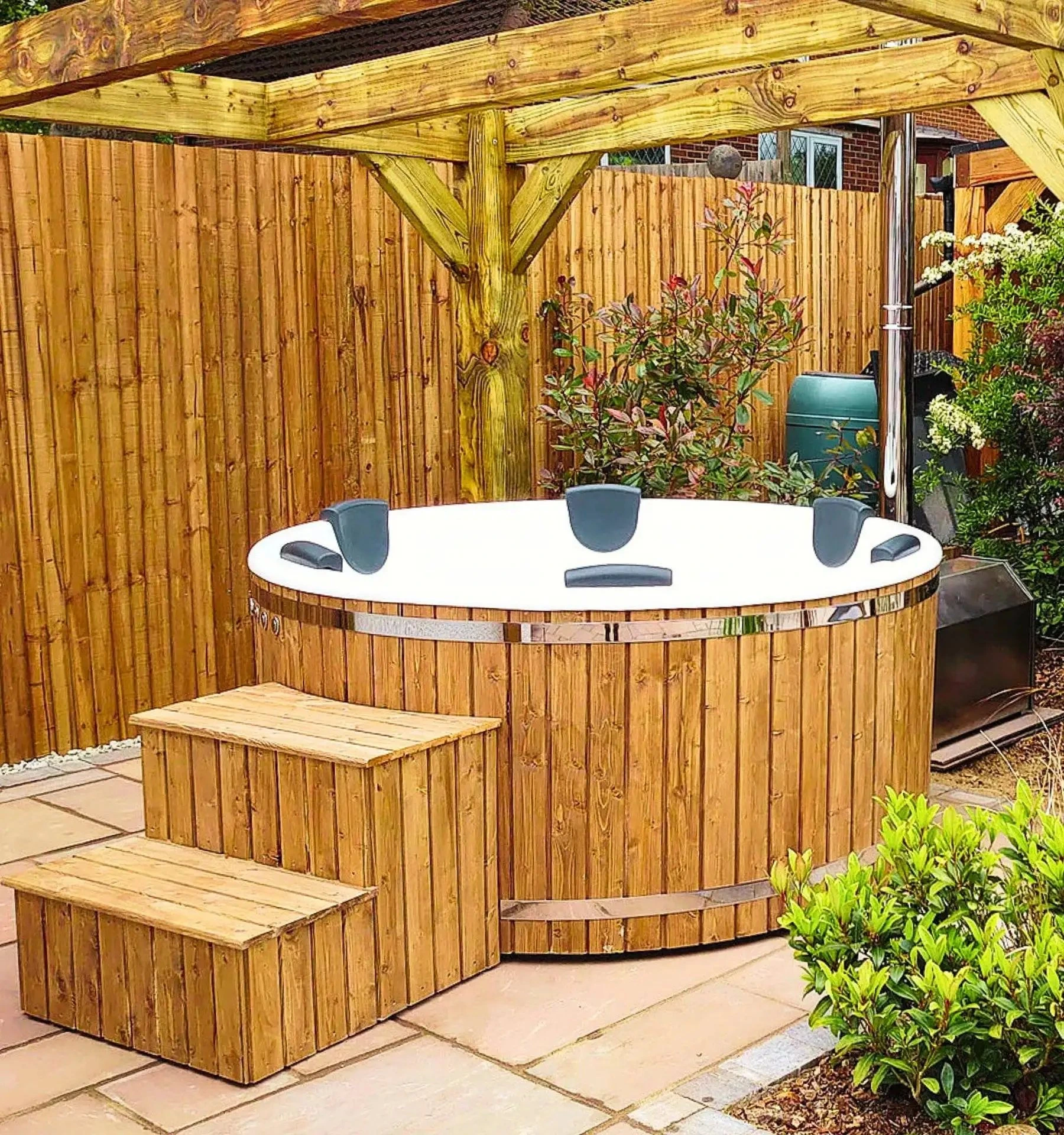 Badestamp i tre med hvitt kar, nakkeputer og tretrapp under en pergola