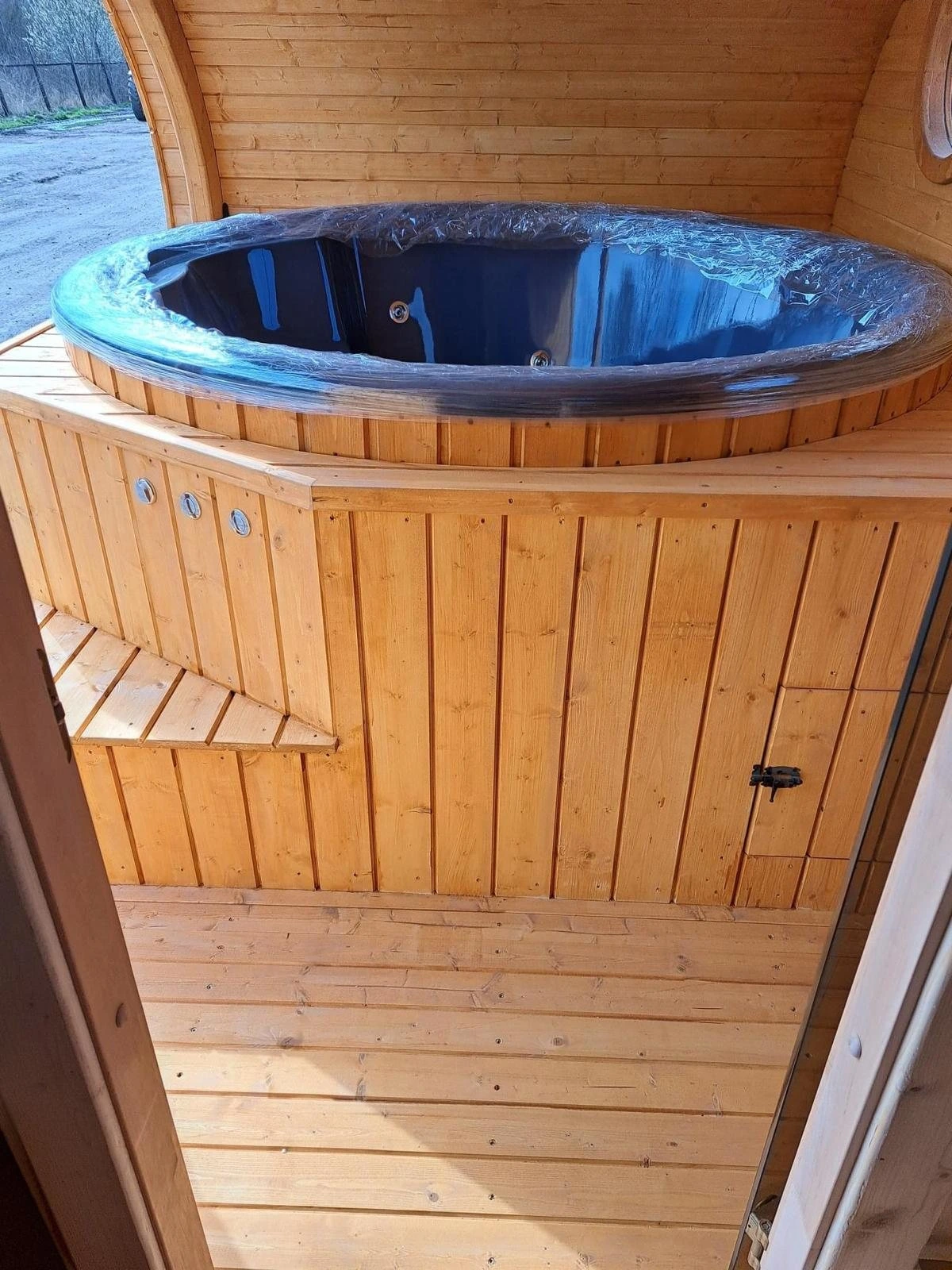 Badestamp med mørkt kar bygget inn i treverket i en badstue, med trinn og tregulv