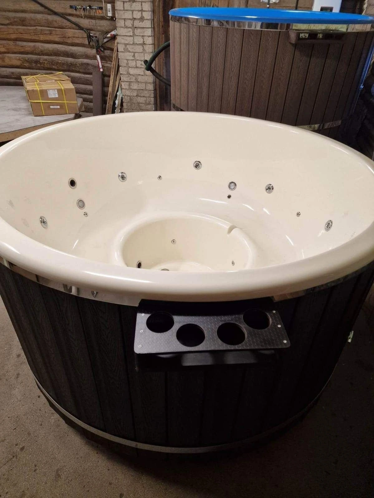 Badestamp med kremhvitt kar og koppholder i stål montert på den mørke kledningen