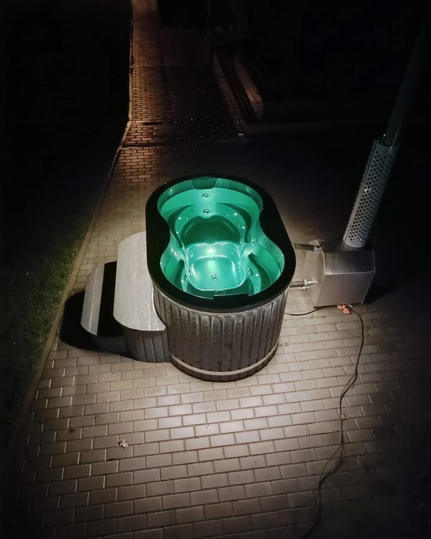 Oval badestamp med grønn innvendig belysning og trapp, fotografert om kvelden