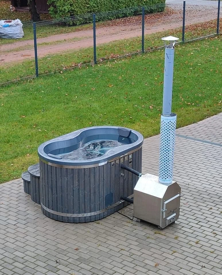Oval badestamp med utvendig vedovn og høy pipe med beskyttelsesgitter