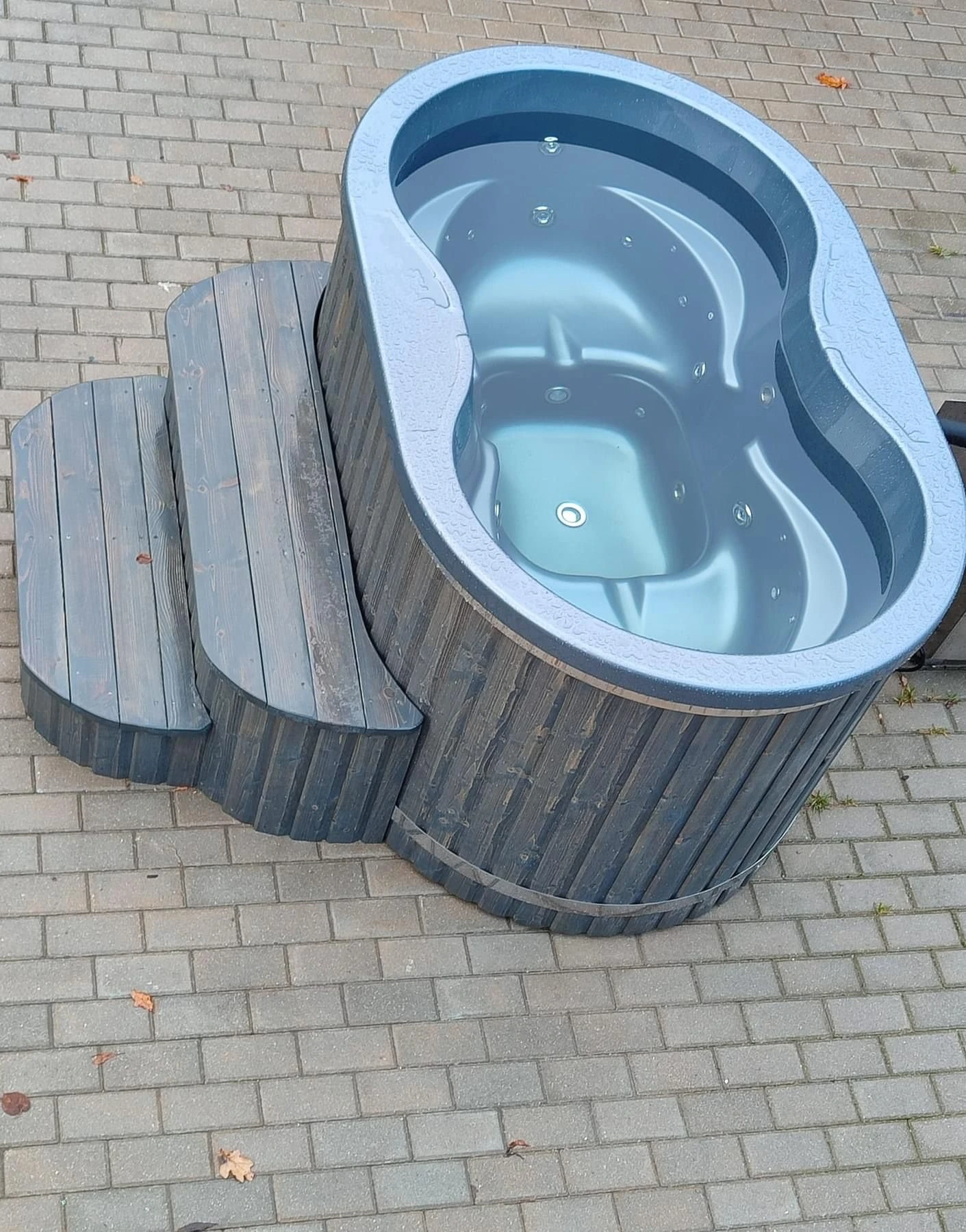 Oval badestamp med lyseblått kar fylt med vann og trapp i gråbeiset tre