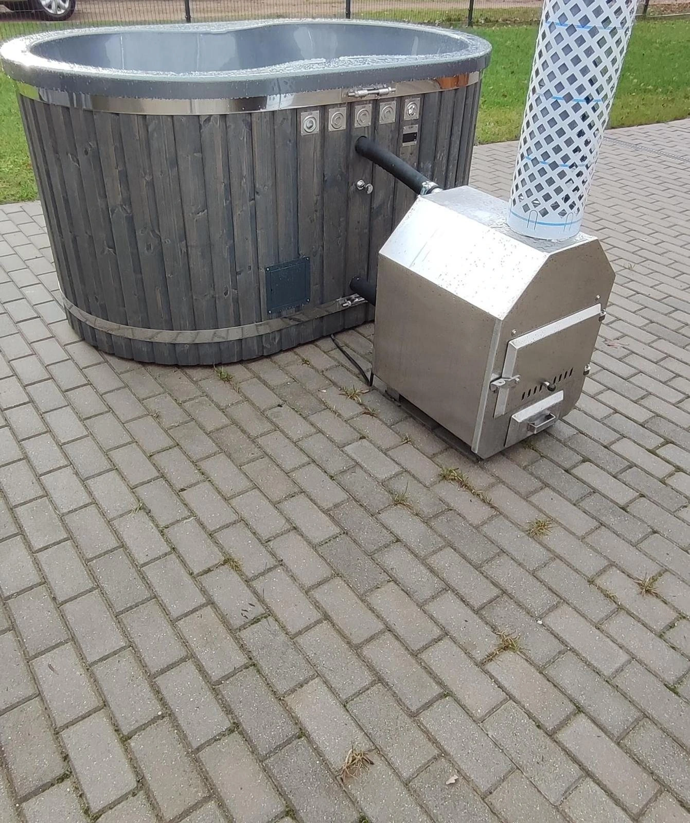 Oval badestamp med mørk trekledning og utvendig vedovn i rustfritt stål